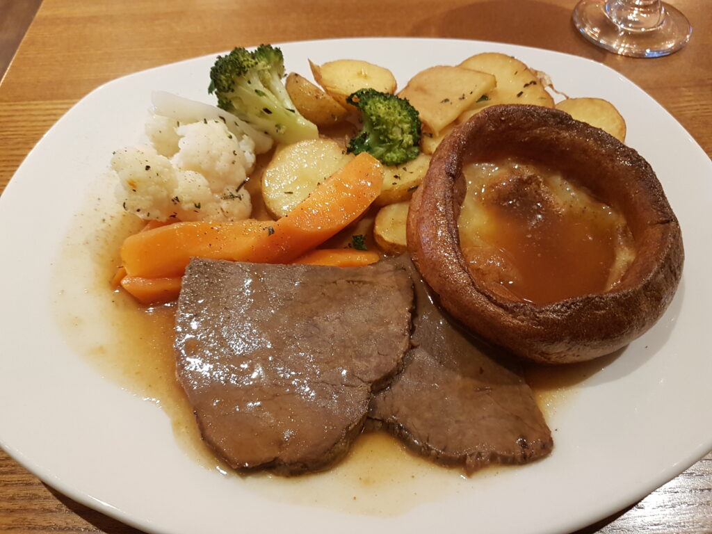 A photo of a plate with roast meat, baked carrots, cauliflower and a yorkshire pudding.